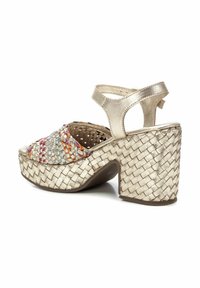 Sandalia de plataforma de metal dorado trenzado con acentos multicolores, tacón de bloque grueso y correa ajustable en el tobillo. Detalle trenzado texturizado en la suela.