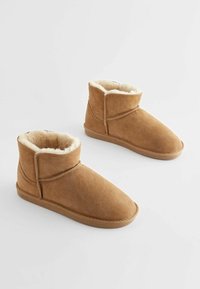 Smeđe suede gležnjače s mekim, kremastim krznom unutra, zaobljenim vrhom i niskom ravnom gumenom potplatom. Minimalne šavove na vanjskom dijelu.