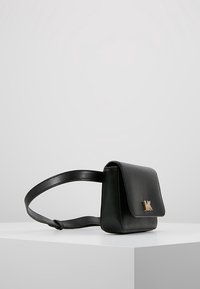 Bolso cruzado de cuero negro con cierre de solapa, acento de logo dorado en la parte delantera y una textura suave. Cuenta con una correa ajustable.