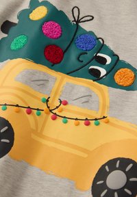 Geel voertuigafbeelding met een groene kerstboom en kleurrijke pompons op een grijze stoffen achtergrond. Geweven accenten overal.