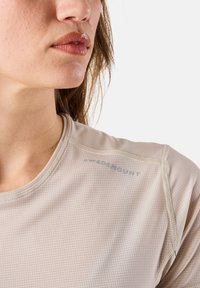 Maglietta atletica beige a maniche corte con un motivo a griglia, con la scritta blu "SWEDENHUNT" vicino alla spalla e cuciture piatte per il comfort.