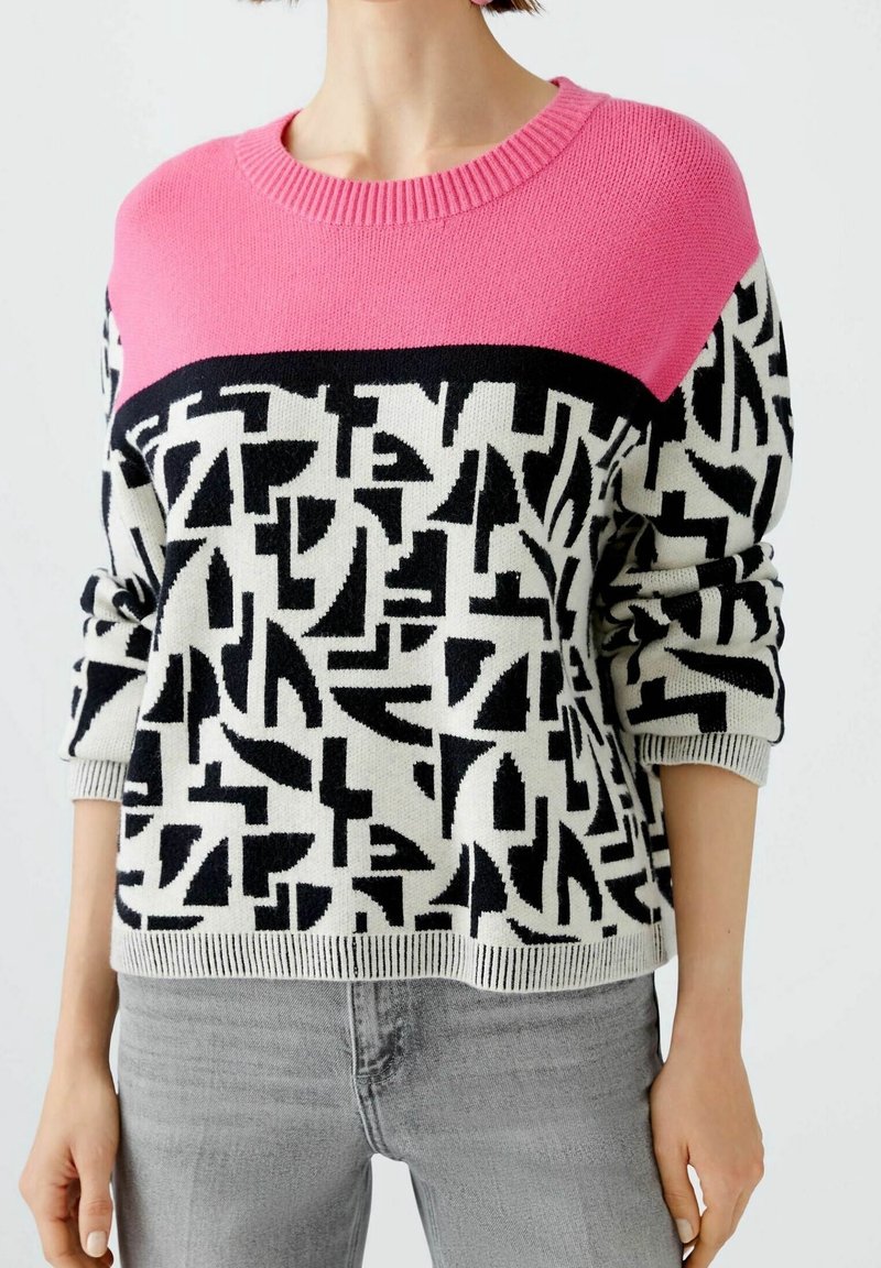 Pull tricoté comportant une section supérieure rose, un motif abstrait noir et blanc en dessous, des manches longues et des poignets et un ourlet côtelés.