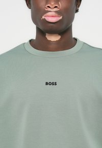 Light green sweatshirt featuring a crew neck, ribbed collar, and a black "BOSS" logo in the center. Soft fabric with smooth texture.