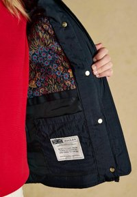 Geacă matlasată de culoare bleumarin cu căptușeală cu model floral, închidere prin capse și buzunar interior cu etichetă. Textură netedă, design practic.