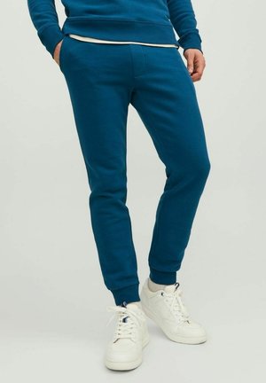 Pantaloni tuta turchesi con vita e polsini a coste, dotati di tasche laterali e realizzati in un morbido materiale misto cotone. Abbinati a sneaker bianche.
