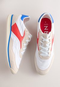 Fehér bőrből és bézs színű velúrból készült sportcipő piros és kék részletekkel, texturált felülettel, kerek orral és fehér fűzővel. Piros talpbetét "FOREVER COMFORT" felirattal.