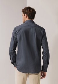 Donkerblauw overhemd met knopen, voorzien van een subtiel geometrisch patroon, lange mouwen en een getailleerde pasvorm, met manchetknoopjes en een afgeronde zoom.