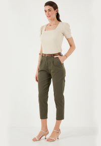 Top beige a costine con scollatura a forma quadrata, maniche a sbuffo; pantaloni verde oliva a vita alta; cintura marrone; décolleté nudi con cinturino; stile minimalista.