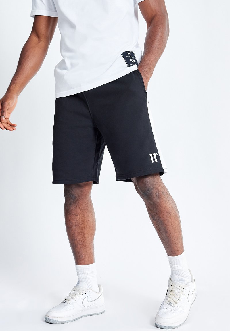 Shorts deportivos negros con una franja lateral blanca, cinturilla elástica y un logotipo impreso. Combinados con zapatillas blancas y calcetines.