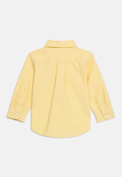 Camiseta amarilla de manga larga para niño pequeño con puños abotonados, cuello y pliegue trasero, mostrada extendida sobre un fondo blanco.