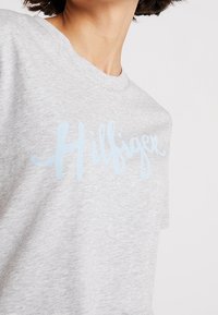 Camiseta de algodón gris con el logo cursivo "Hilfiger" en azul claro en el frente. Diseño de cuello redondo, mangas cortas y corte relajado.