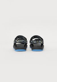 Sorte sandaler med mønstrede justerbare stropper og blå såler, som har en teksturert fotsoff og en lett design for komfort.