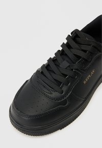 Adidași negri din piele sintetică, cu perforații accentuate pe vârf, șireturi plate negre și logo-ul "REPLAY" în aur.
