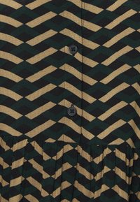 Abito abbottonato con un motivo a zigzag in verde e oro su uno sfondo nero, con gonna plissettata e bottoni neri.