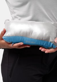 Compact kussen met een glanzend zilveren bovenkant en een blauwe stoffen onderkant. Beschikt over een rits en de tekst "STOW AWAY" aan de zijkant, met een zachte textuur.