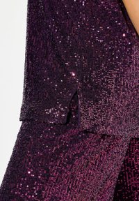 Pailletteret outfit med en lilla ombre-effekt, der har en struktureret overflade, små slids og overlappende lag, som øger det visuelle detalje.
