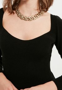 Black ribbed knit top with a square neckline and long sleeves, paired with a chunky gold chain necklace.
