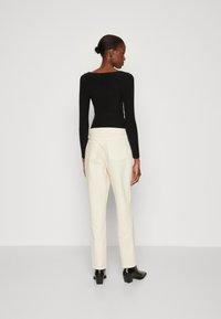 Haut noir à manches longues et côtelé associé à un pantalon droit couleur crème, doté de deux poches arrière et de bottines à talons noirs.