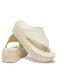 Sandali Crocs beige con una piattaforma spessa, cinturini regolabili e una soletta testurizzata. Dettaglio del logo rinforzato sul lato. Finitura liscia.