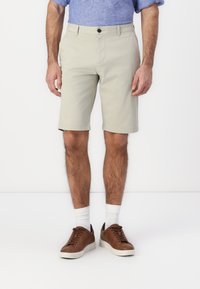 Beige bomullshorts med rett snitt, frontlommer og brettet hem. Kombinert med brune joggesko og hvite sokker.