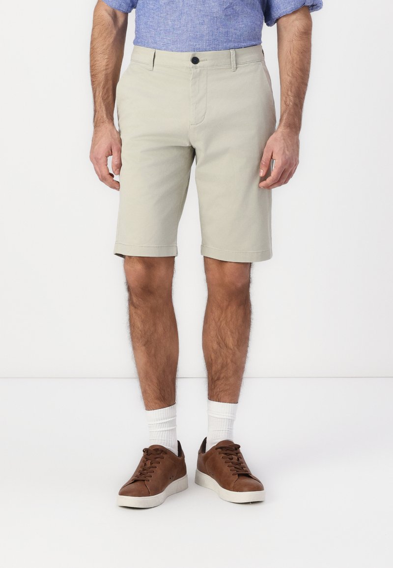 Beige bomullshorts med rett snitt, frontlommer og brettet hem. Kombinert med brune joggesko og hvite sokker.