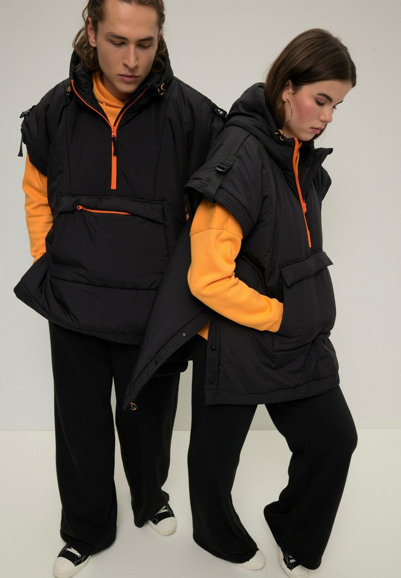 Giubbotti neri imbottiti con cerniere e dettagli arancioni, dotati di cappucci oversize, tasche a marsupio e pantaloni neri larghi.