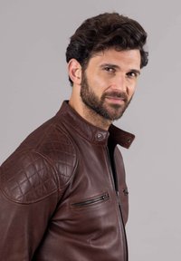 Brown leather jacket with a zip closure, quilted shoulder patches, and two zippered chest pockets. Smooth texture and fitted design.
