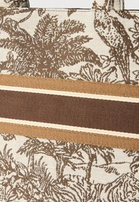 Textil táska krémszínű háttérrel és barna botanikai mintákkal, amelyeket különböző szélességű barna és bézs vízszintes csíkok díszítenek.