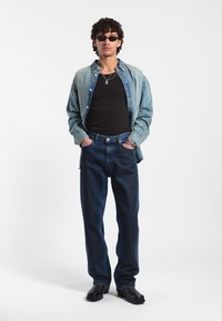 Džínová košile vrstvená přes černý top na ramínka, spárovaná s tmavě modrými džíny a černými botami. Doplněno vrstvami řetězů a slunečními brýlemi.