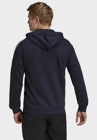 Sudadera navy con bolsillo tipo canguro, puños y dobladillo acanalados. Cuenta con capucha con cordón y franjas laterales en contraste. Textura de tela suave.