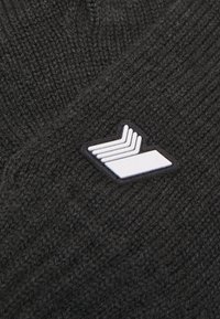 Mustmust mesitar, millel on valge logo silt, kus on kolm paralleelset joont, lisades tekstuuri ja detaile üldisele disainile.