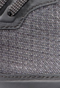 Grå sneakersko med texturerad tygövre, ett vävt mönster och släta syntetiska detaljer. Sömmar synliga längs kanten.