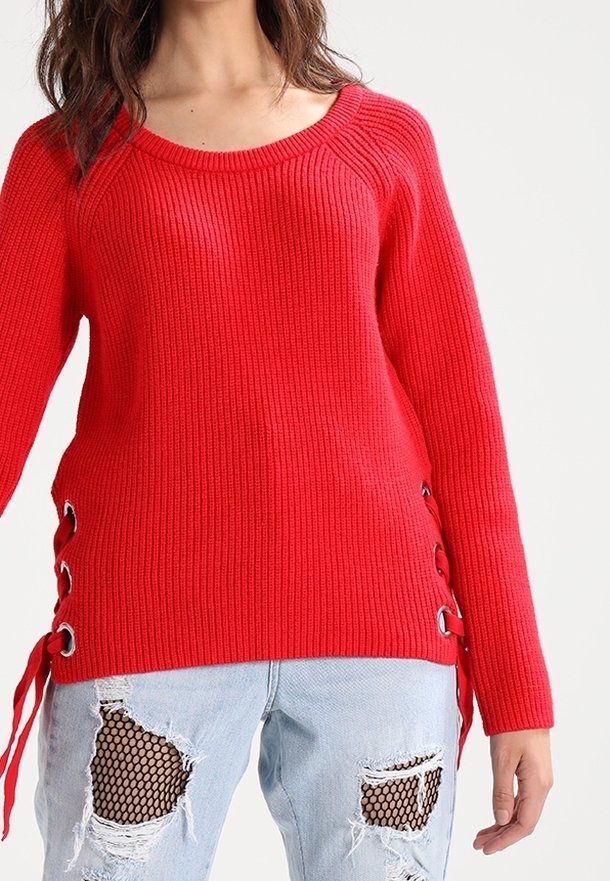 Red ribbed sweater with long sleeves and side lace-up details. Paired with light blue distressed jeans featuring mesh patches and frayed hems.