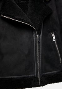 Giubbotto in shearling nero con colletto distintivo, zip frontale e dettagli in pelle. Presenta una texture morbida e un design elegante.