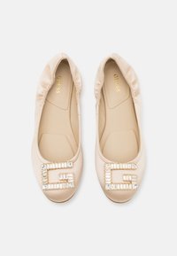 Ballerine in satin beige con soletta imbottita, caratterizzate da un grande logo "G" incastonato di strass sulla punta. Texture liscia.