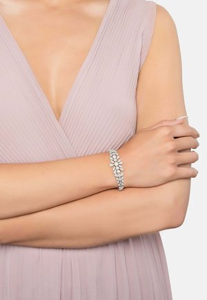 Silver bracelet with floral and leaf designs, featuring clear rhinestones. Worn on a bare arm, paired with a light mauve pleated dress.