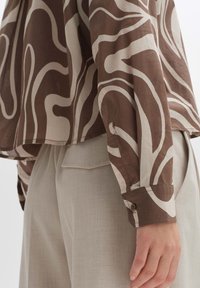 Brown and beige patterned shirt with a relaxed fit, long sleeves, buttoned cuffs, and smooth, lightweight fabric. Paired with light trousers.