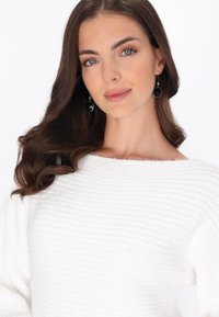 Pulover alb tricotat cu dungi, cu o decolteu larg. Modelul poartă cercei negri lungi și circulare. Textură netedă și design cu un croi lejer.
