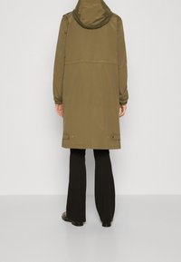 Wasserfester Mantel in Olivgrün mit Kapuze, ausgestattet mit langen Ärmeln, geradem Schnitt und verstellbaren Kordelstoppern am Saum zur Anpassung der Passform.