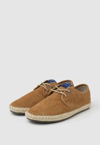 Zapatos de ante marrón con punta redondeada, suela de cuerda trenzada beige y dos ojales para los cordones; diseño minimalista con etiquetas azules.