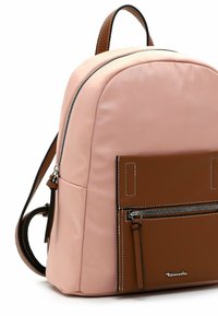 Rosa Rucksack mit einer runden Form, ausgestattet mit einer vorderen Tasche aus braunem Leder, silbernem Reißverschluss und kontrastierenden Nähten.