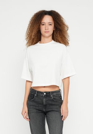 Weißes kurzes T-Shirt mit kurzen Ärmeln und Rundhalsausschnitt, kombiniert mit dunkelgrauen, hoch taillierten Jeans. Glatter Stoff ohne sichtbare Muster.