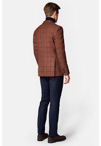 Brązowa marynarka w kratę, wykonana z teksturowanej tkaniny, zestawiona z granatowymi spodniami. Wyróżniające się szczegóły to dopasowany krój i zapięcie na jeden guzik.