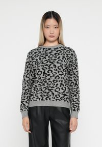 Un pull gris avec un imprimé léopard noir, col ras du cou et poignets côtelés, fabriqué en matériau tricoté épais, associé à un pantalon en cuir noir.
