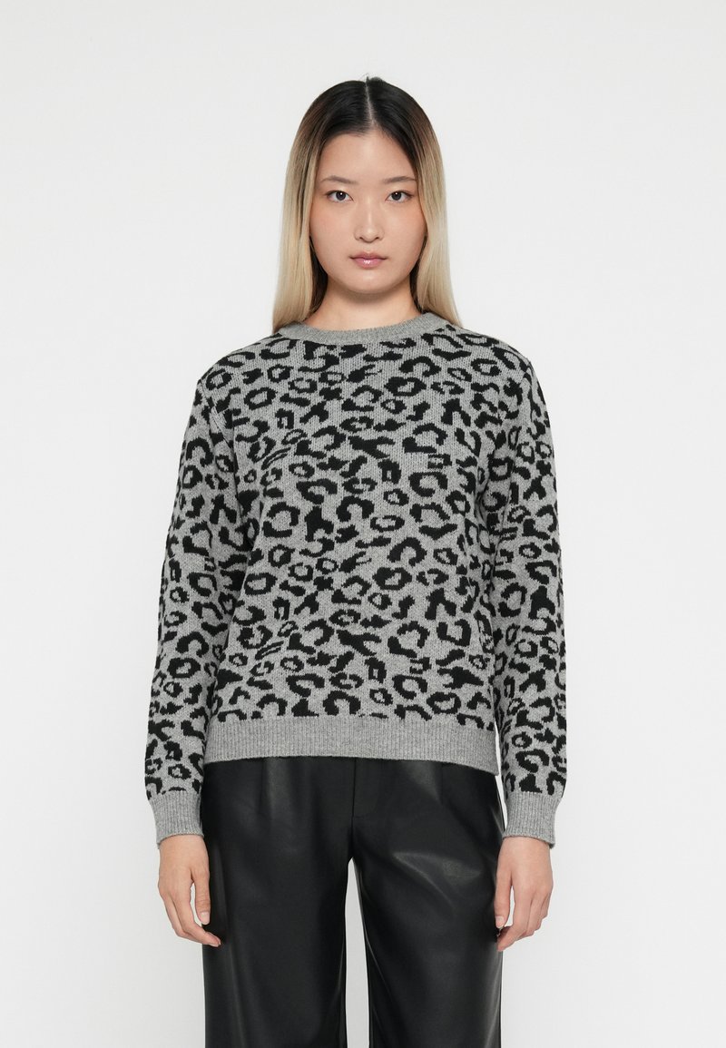 Un pull gris avec un imprimé léopard noir, col ras du cou et poignets côtelés, fabriqué en matériau tricoté épais, associé à un pantalon en cuir noir.