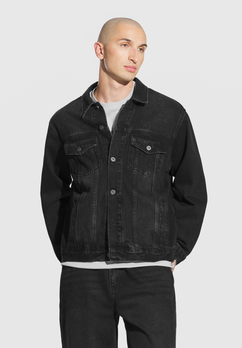 Czarna kurtka dżinsowa o klasycznym fasonie, z zapięciem na guziki, dwoma kieszeniami na piersi i lekko przetartą teksturą.
