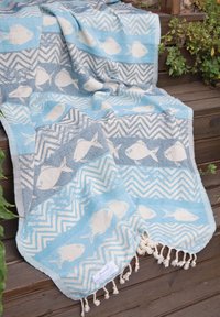 Blue and white patterned woven blanket with fish and zigzag designs, draped over wooden steps with nearby green plants.