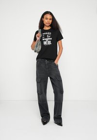 Čierne tričko s výrazným bielym textom, v kombinácii s voľnými tmavými cargo nohavicami s vreckami a šedou kabelkou s textúrou. Čierne lodičky.