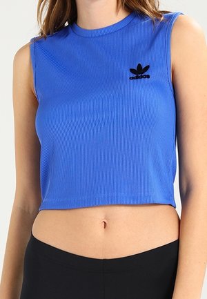 Ärmelloses, blaues, kurz geschnittenes, geripptes Top mit schwarzem Adidas-Logo, getragen zu schwarzen, hoch taillierten Unterteilen, die den Bauch freilegen.