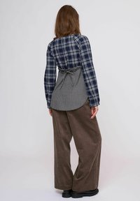 Kockás ing tengerészkék és fehér színekben, kockás mintával a hátoldalán, barna bőszárú kordbársony nadrággal és fekete csizmával párosítva.